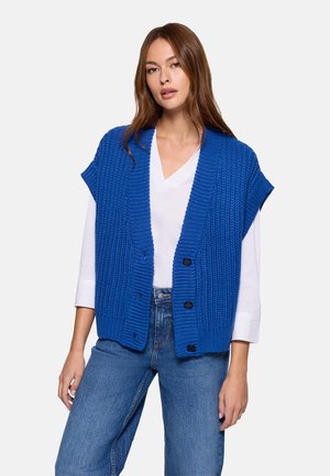 Chaleco de punto azul con textura acanalada, abertura frontal y mangas cortas, con botones negros y llevado sobre una camisa blanca.