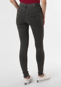 Jeans ajustados de talle alto en gris, con cinco bolsillos, detalles de costura sutiles y una textura de mezclilla suave, combinados con zapatillas blancas.