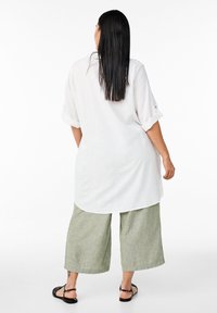 Bela lanena srajca z zavihanimi rokavi, v kombinaciji s svetlo zelenimi širokimi hlačami. Sandali s tankimi trakovi, gladko teksturo in sproščenim krojem.