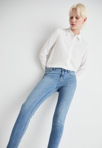 Fehér, gombos, klasszikus ing, világoskék slim fit farmernadrággal párosítva. Sima szövettextúra, egyszerű dizájn, látható minták nélkül.
