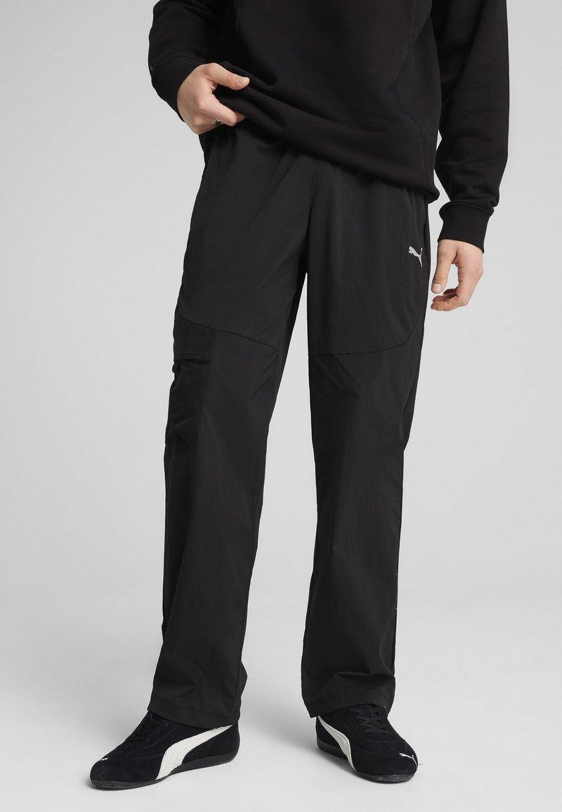 Melni sporta bikses ar brīvu piegriezumu, ar kabatu ar rāvējslēdzēju, vieglu audumu un diskrētu logotipa akcentu sānos.