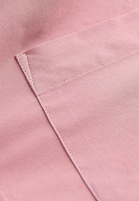 Gros plan sur une poche en tissu rose avec des coutures visibles sur un tissu à texture lisse.