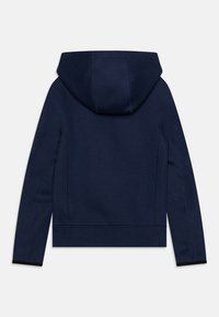 Námořnická modrá mikina s kapucí vyrobená z měkké tkaniny. Obsahuje klokankovou kapsu, žebrované manžety a švy podél stran.