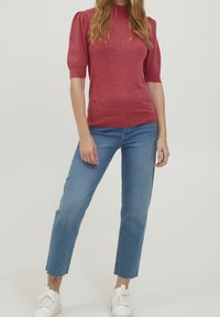 Röd kortärmad stickad tröja med hög halsringning och puffärmar, i kombination med avklippta blå jeans och vita sneakers.