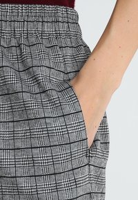 Pantalones con estampado en blanco y negro, con cintura elástica y bolsillos laterales, que presentan un diseño de rejilla texturizada.