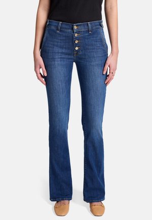 Jean flare bleu en denim haut de gamme avec fermeture à bouton, cinq poches et une finition lavée moyenne. Texture lisse avec un léger stretch.