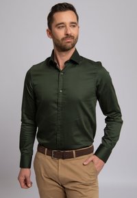 Groen satijnen overhemd met een puntige kraag en lange mouwen, voorzien van een knoopsluiting aan de voorkant en een gladde textuur, gecombineerd met khakibroek.