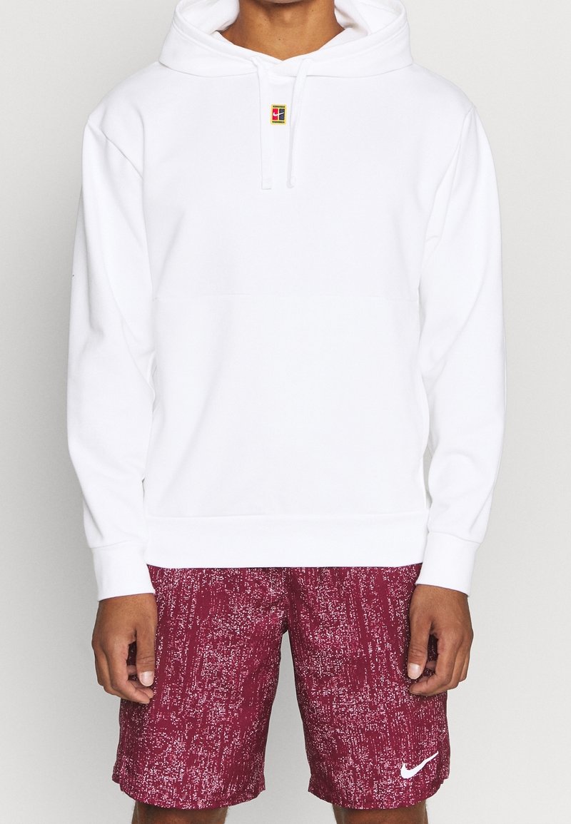 Sweat à capuche blanc avec poche avant, capuche ajustable et petit logo coloré au centre de la poitrine. Associé à un short bordeaux présentant un motif texturé.