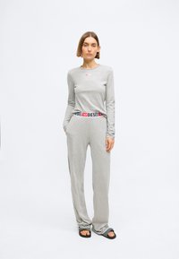 Sivi dugi rukav majica s malim crvenim logotipom, u kombinaciji sa sivim hlačama koje imaju crnu i crvenu markiranu pojas. Nosi se uz crne papuče.