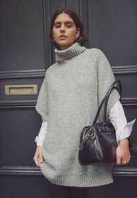 Maglione lavorato a maglia oversized di colore grigio chiaro con colletto alto e maniche corte. Abbinato a una borsa a tracolla in pelle nera.