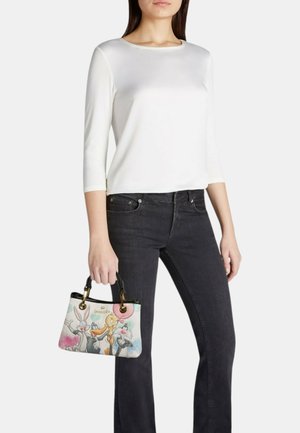 Vrouw draagt een wit topje met lange mouwen en zwarte jeans en houdt een kleine handtas met een print van Bugs Bunny, Tweety en Sylvester vast.