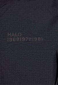 Čierna látka s mriežkovou textúrou obsahuje potlač "HALO 196819721981" v svetlejšej farbe. Minimalistický dizajn s čistými liniami.