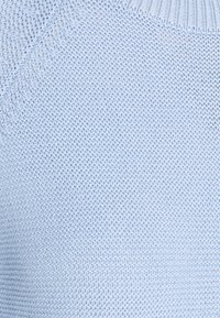 Ljusblått stickat tyg med ett strukturerat mönster och ribbad halsringning. Materialet verkar mjukt och något elastiskt.