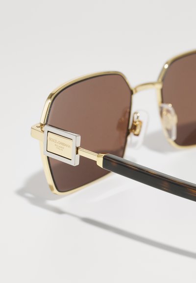 Brown lens sunglasses with gold metal frames, tortoiseshell temples, and silver accents. Features a logo plate on the frame.