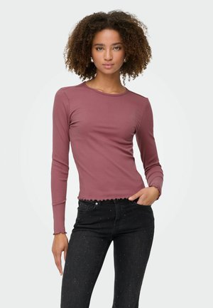 Langärmliges, eng anliegendes Rippoberteil in Mauve mit gewelltem Saum und Bündchen, kombiniert mit schwarzen Jeans, die verstreute metallische Akzente haben.