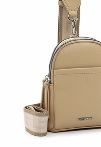 Beige leather crossbody bag with a rounded shape, featuring a zip closure, front pocket, and a textured woven strap with a patterned accent.