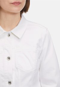 Weiße Jeansjacke mit klassischem Kragen, silbernen Druckknöpfen und zwei Brusttaschen mit strukturiertem Finish.