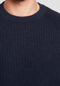 Maglione a coste blu navy con scollo rotondo e motivo testurizzato, che presenta leggere variazioni di colore e un design aderente.
