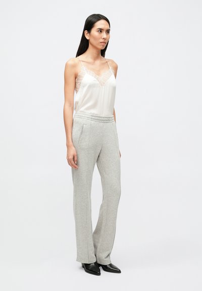 Biely saténový cami top s čipkovaným lemom v kombinácii so sivými pružnými joggermi. Joggery majú bočné vrecká a zužujúci sa strih. Čierne lodičky s špicatou špičkou.