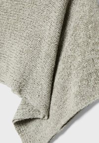 Primo piano di tessuto lavorato a maglia grigio chiaro con motivo testurizzato ad anelli e pieghe visibili che creano ombre.