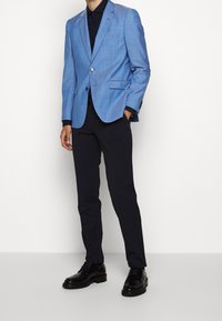 Blazer azzurro chiaro in tessuto texturizzato, chiusura a un bottone, abbinato a pantaloni scuri e scarpe stringate nere.