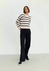 Crèmekleurige trui met zwarte strepen, gecombineerd met hoog getailleerde zwarte jeans en zwarte sneakers. Glad gebreide textuur, casual pasvorm.