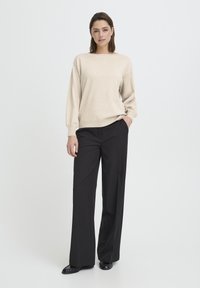 Bézs kötött pulóver széles nyakkivágással és hosszú ujjakkal, fekete szabott nadrággal párosítva. Sima textúra, kényelmes szabás és minimalista dizájn.