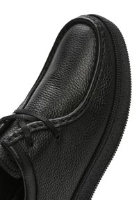 Chaussure en cuir noir avec une surface texturée, bout arrondi, accents cousus et semelle en caoutchouc avec une adhérence texturée.