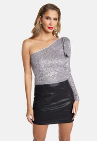 Sølvpailetteret top med én skulder, parret med en tætsiddende sort miniskirt. Stoffet har en blank, glat tekstur og et struktureret design.