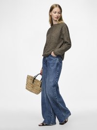 En brun stickad tröja med rund halsringning, i kombination med vida blå denimjeans. Bär en vävd halmficka med svarta handtag.