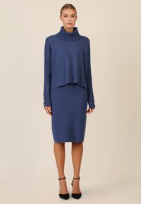 Completo lavorato a maglia blu navy composta da un top con collo a imbuto e maniche a coste, abbinato a una gonna a matita aderente. I dettagli includono bottoni sulle maniche.