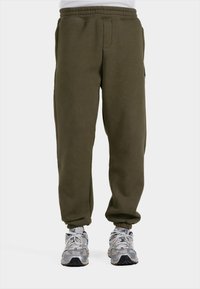 Groene, dikke sweatpants met een elastische tailleband, twee voorkruiden en elastische boorden bij de enkels. Gecombineerd met lichtgrijze sneakers.
