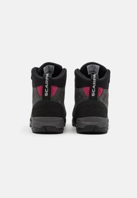 Botas de senderismo en negro y gris con un acento rosa. Material de ante y malla, altura hasta la pantorrilla, suela texturizada y logo prominente en el talón.
