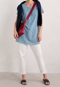 Sininen tunika, jossa on kukkakuosi, valkoiset housut, tummansininen neule hartioilla ja viininpunainen olkalaukku. Kengät ovat sinisiä, joissa on remmit, ja ne täydentävät asun.