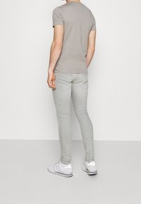 Camiseta gris claro y jeans ajustados gris claro. La camiseta tiene un cuello redondo, y los jeans cuentan con bolsillos traseros y una textura desgastada. Zapatillas blancas.