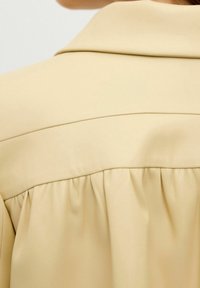 Primo piano della parte posteriore di una giacca in pelle beige che mostra il dettaglio della yoke e la cucitura arricciata sotto la cucitura della spalla.