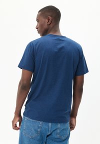 Tamsiai mėlyna crew-neck tipo marškinėliai su trumpomis rankovėmis, pasižyminčiais tekstūruotu audiniu ir patogiu siluetu, derinami su šviesiai mėlynomis džinsinėmis kelnėmis.