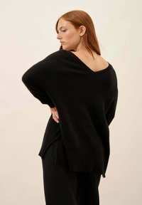 Černý oversized svetr s výstřihem do V a otevřeným zadním dílem. Vyroben z texturovaného pleteného materiálu. Má kleslé ramena a postranní rozparky.