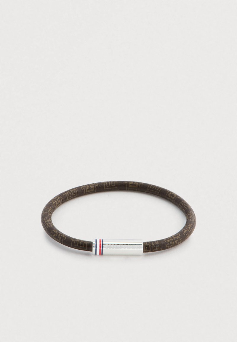 Rjav zapestni trak iz gume z vzorcem in srebrnim kovinskim dodatkom z rdečimi in modrimi črtami. Okrogla oblika, gladka tekstura.