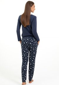 Granatowa bluzka z długim rękawem w połączeniu z dopasowanymi spodniami w biały wzór gwiazdek na ciemnym tle. Miękki materiał o gładkiej fakturze.