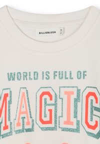 Witte katoenen t-shirt met de tekst "DE WERELD IS VOL MAGIE" in groene glitter en koraal blokletters, ronde halslijn en ribgebreide kraag.