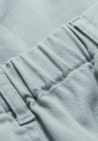 Tissu bleu clair avec une texture côtelée, doté d'une taille élastique froncée et de coutures visibles. Apparence douce et lisse.
