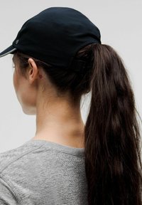 Svart keps med en texturerad yta och justerbar rem baktill, som kombineras med en grå kortärmad skjorta med ett subtilt mönster.
