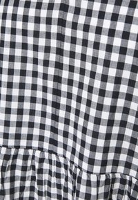Tissu vichy noir et blanc avec petit motif à carreaux et détail de couture froncée.