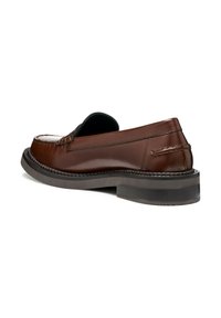 Zapato de piel marrón tipo slip-on con punta redondeada, costuras en contraste y una suela de goma semitransparente y baja. Acentuado con un talón ligeramente elevado.