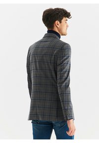 Marynarka w kratę w odcieniach szaro-niebieskich, charakteryzująca się klasycznym krojem, klapami oraz detalem czterech guzików na mankietach. Tekstura materiału w wzory.