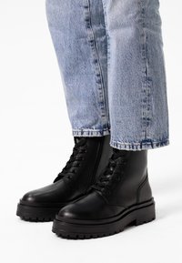 Bottes de combat en cuir noir avec une semelle épaisse, bout rond et lacets, assorties à un jean bleu clair retroussé.