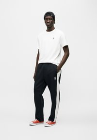 Λευκό μπλουζάκι, μαύρο αθλητικό παντελόνι με λευκές πλευρικές ρίγες, κόκκινα αθλητικά παπούτσια, μαύρο καπέλο με μπλε ρίγες, μικρό λογότυπο στο μπλουζάκι.