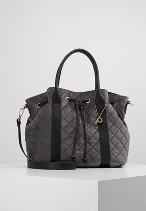 Sac à main matelassé gris avec poignées et sangles en cuir noir, œillets dorés pour cordon et un petit pendentif suspendu sur une surface blanche.