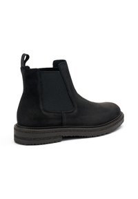 Stivale Chelsea in suede nero con pannello elastico laterale, punta rotonda e suola in gomma testurizzata. Presenta un tassello sul retro per una facile calzata.